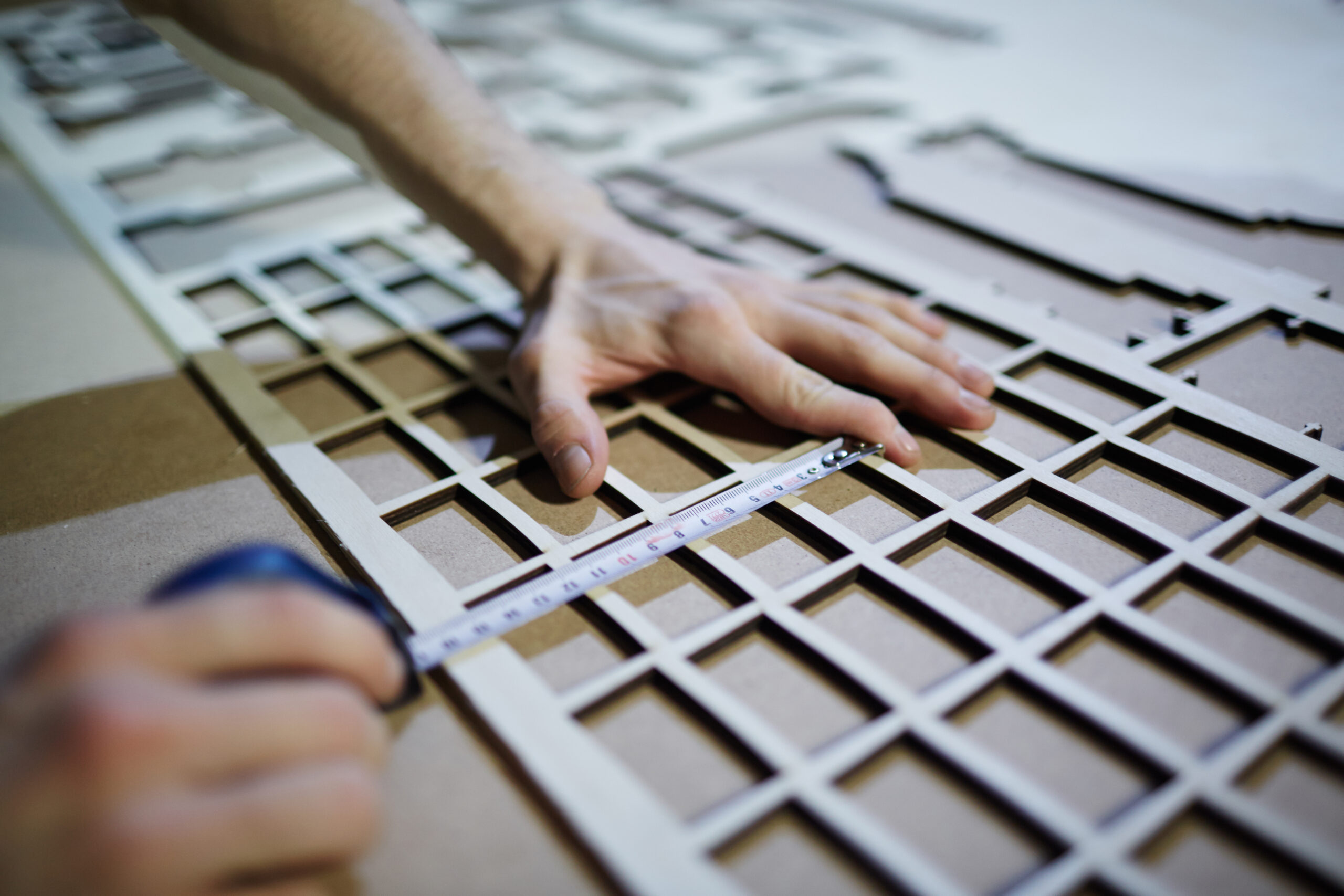 Hands of craftsman measuring plywood sheet with cut cells
